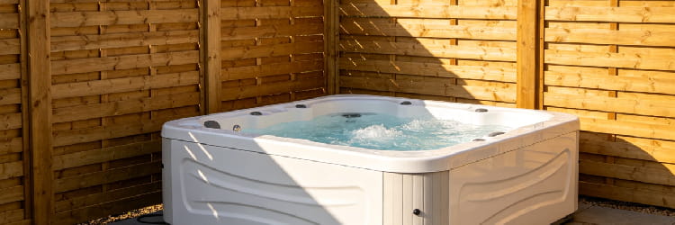 Outdoor white hot tub with hydrotherapy jets, bubbling water in a wooden privacy enclosure.png
